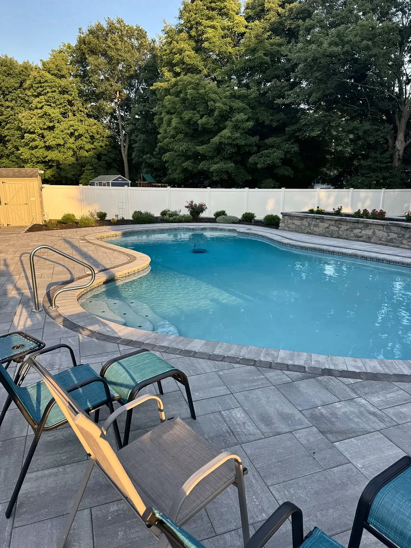 Free-form pool ringed by gray pavers and a dark border in Reading, MA
