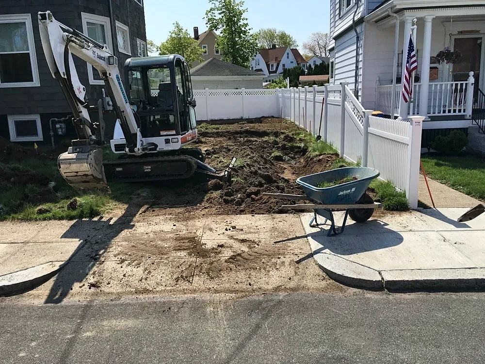 Mini excavator digging out soil in a front yard at the start of a hardscape job