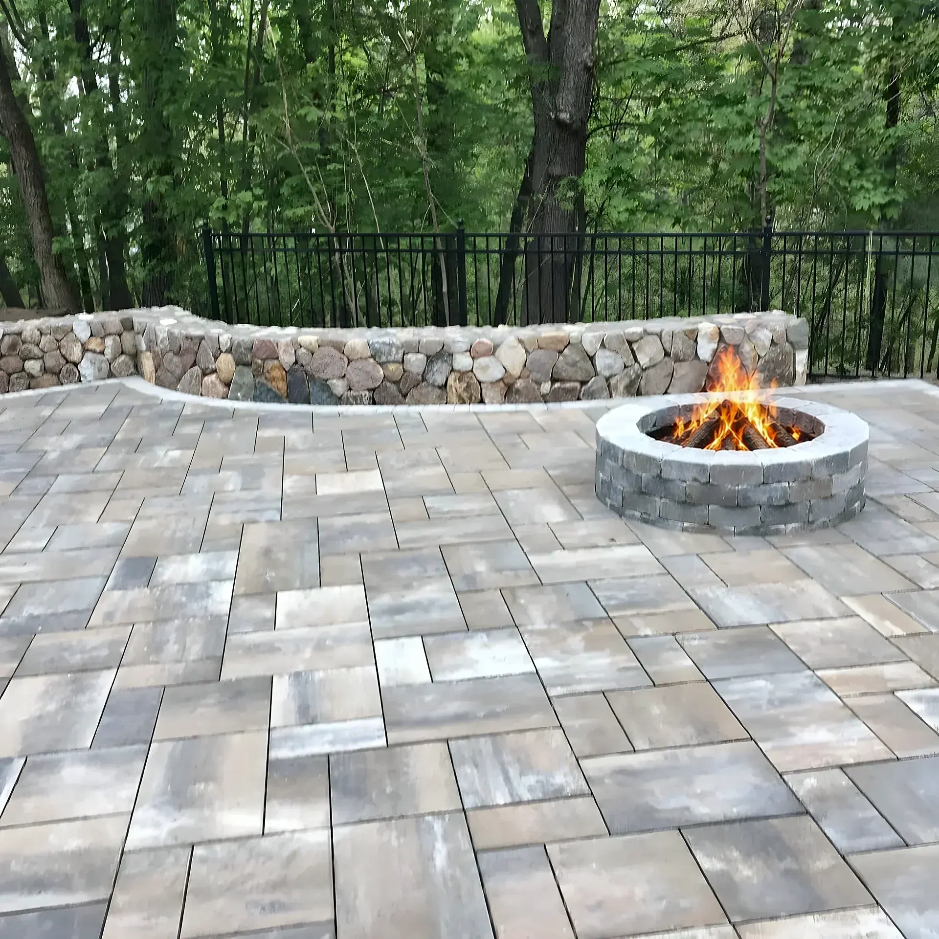Paver patio with a round stone fire pit, backed by a curved fieldstone wall and black fence