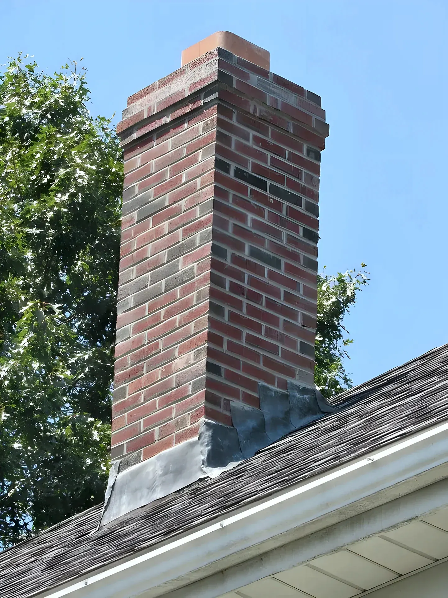 Red brick chimney above a shingled roof with metal flashing at the base