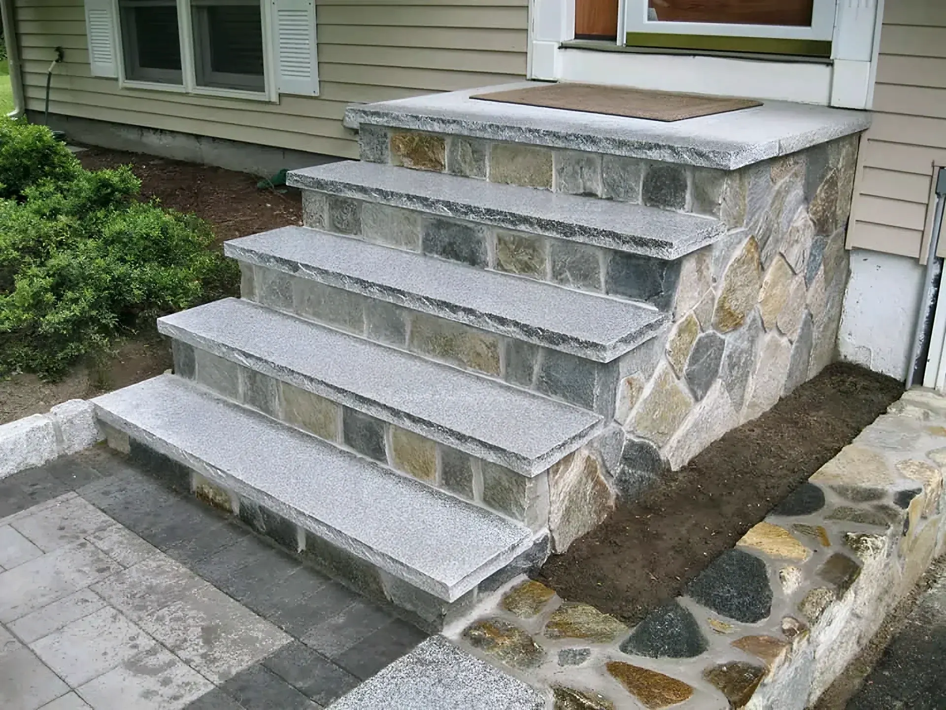 Natural stone veneer steps with thick granite treads and a matching stone planter wall