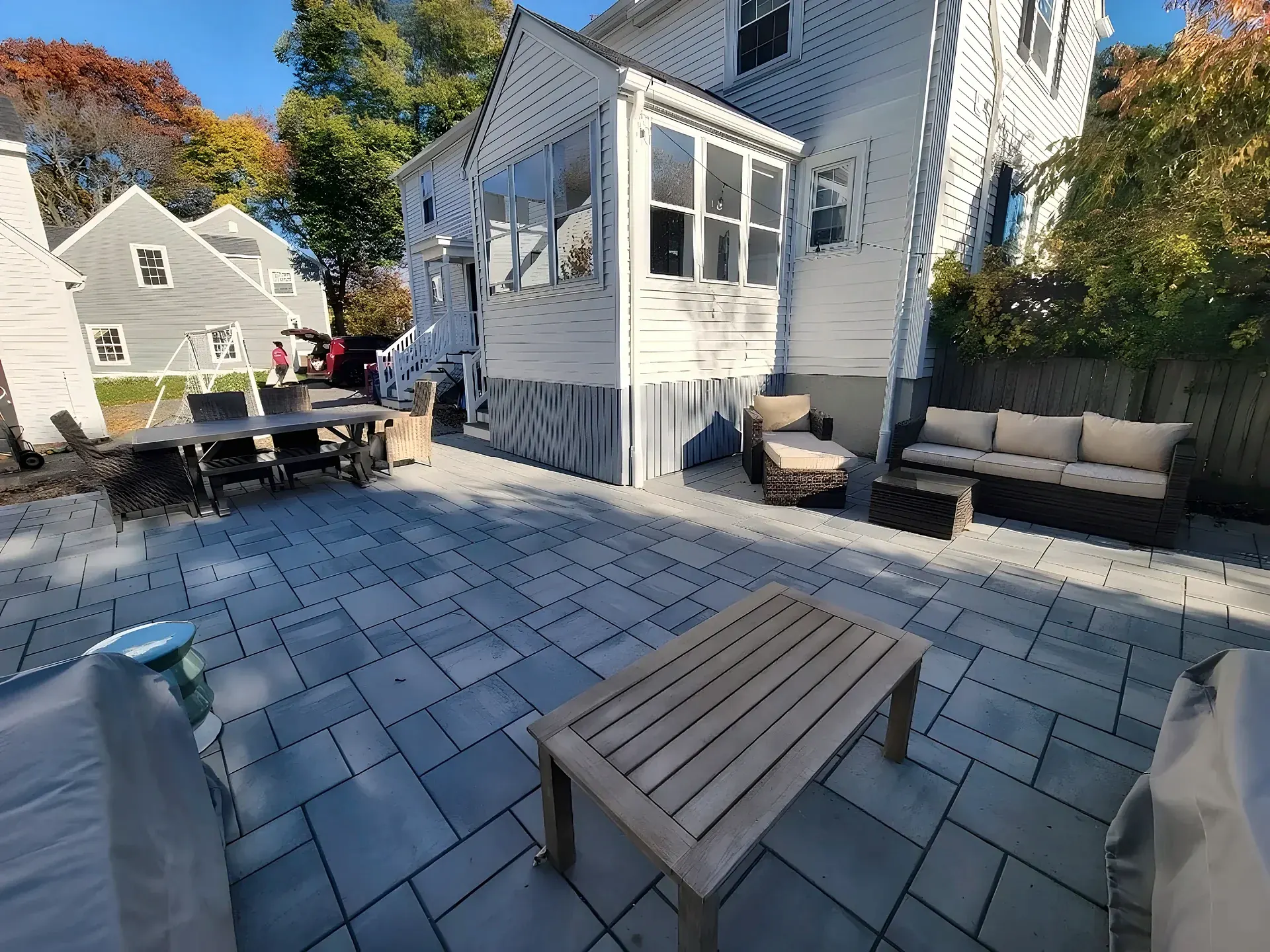 Large gray paver patio next to a house with an outdoor dining table and lounge seating